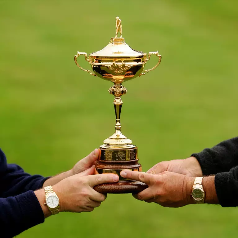 Ryder Cup Trophy being held by 2 men who are wearing Rolex Day-Date watches