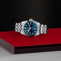 Tudor Black Bay 31 blue diamond dot dial on its side on a black and red background