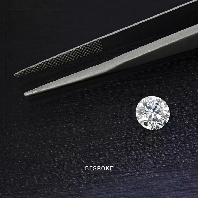 Single loose diamond with precision tweezers on a dark background. Discover our bespoke service