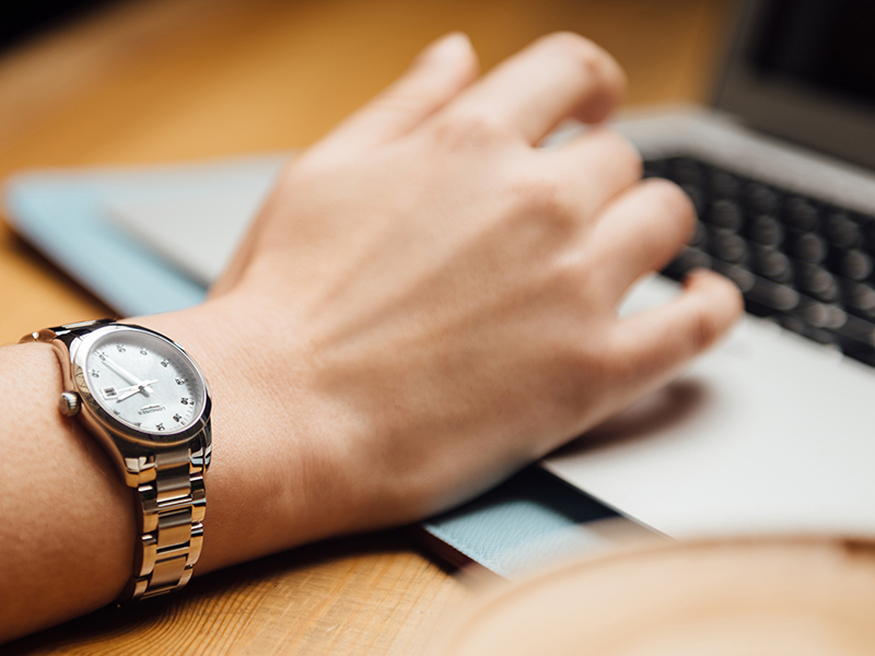 woman wearing a steel with mother of pearl dial longines watch whilst typing on a keyboard